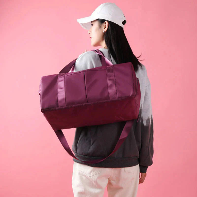 HealthyRealLife maroon waterproof fitness duffel bag carried on shoulder by woman in white cap against pink background